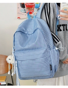 Detail eines blau karierten Schulrucksacks mit Plüschanhänger und großer Reißverschlusstasche
