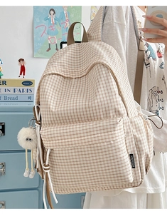 Detail eines beigen karierten Rucksacks mit Plüsch-Anhänger und vorderer Reißverschlusstasche