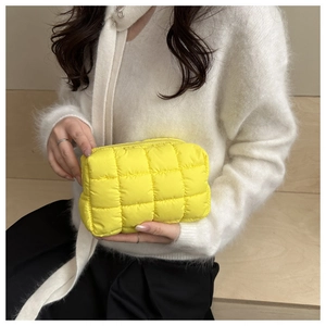 Quilted yellow puffy cosmetic bag held by a model in a cozy white sweater