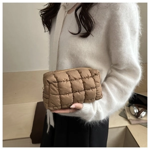 Detail of khaki quilted puffer makeup bag held by model showing grid stitching texture
