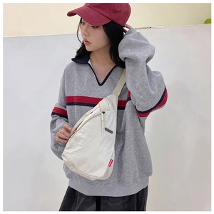 Detail of off-white canvas chest bag with adjustable strap and red logo on model