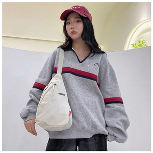 Detail view of a cream crossbody nylon chest bag worn with a retro sporty sweatshirt