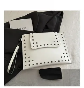 Detailed close-up of white leather envelope clutch with metallic rivet studs and wrist strap