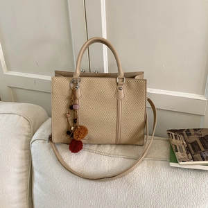 Chic beige woven tote bag with faux leather handles and colorful pom-pom charm on sofa