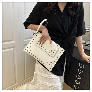 Detail of white envelope bag with dark metal square rivets and slim top handle