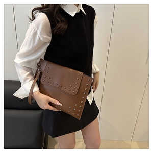 Detail view of brown envelope clutch bag featuring silver studs and detachable wristlet strap
