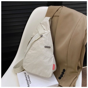 Detail of a beige nylon crossbody bag with metal logo and fashion label on casual wear