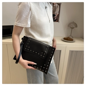 Detail of black envelope clutch featuring silver square rivets and wrist strap