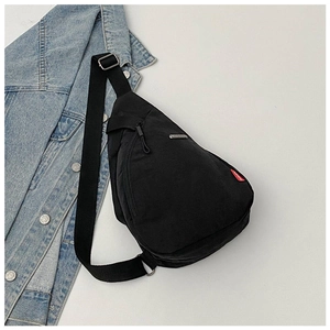 Detail of black nylon chest bag with red label and metal logo next to denim jacket