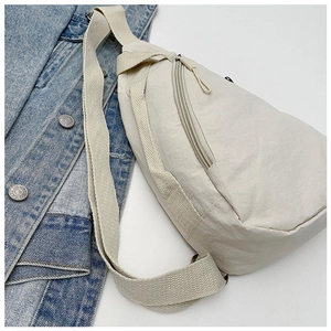 Detail of minimalist cream nylon crossbody chest bag with wide strap on denim jacket background