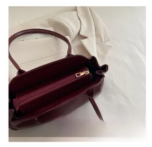 Detail of dark red tote bag featuring internal zipper compartment and gold metal hardware