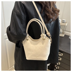 Detail of cream white bucket bag with knot handles and adjustable shoulder strap worn by model