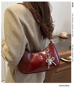 Detalle del bolso hobo de charol burdeos con colgante de lazo plateado y acabado brillante