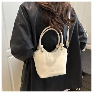 Détail d'un sac seau beige en cuir ciré avec poignée à nœud tressé et anneaux métalliques