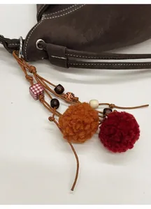 Détail d'un sac en cuir marron foncé avec pompons en peluche colorés et breloques en bois