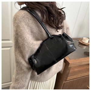 Detailed view of black patent leather shoulder bag on a model wearing beige sweater