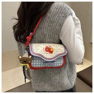 Detail view of plaid shoulder bag with apple print, red piping, and brown bear charm