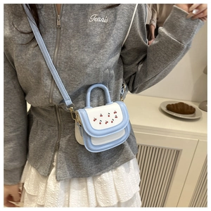 Detail shot of mini crossbody bag featuring red cherry prints and color-block leather texture