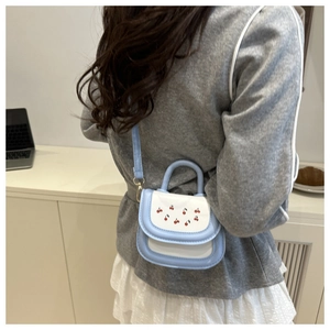 Lifestyle shot of a mini crossbody bag with cherry embroidery on a white and blue leather flap