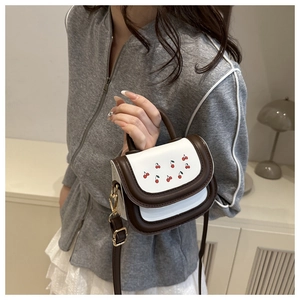 Detail of a white cherry print mini crossbody bag with brown handles and gold hardware