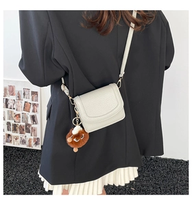 Detail of light gray leather flap crossbody bag with a brown plush monster charm accessory