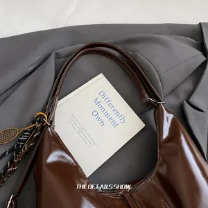 Détail d'un sac cabas en cuir marron brillant avec un charme de raquette de tennis en métal