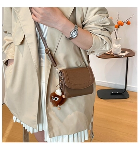 Close-up of brown litchi pattern leather bag with a cute plush doll charm