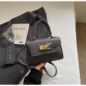 Detalle de bolso trapezoidal gris oscuro con cierre giratorio dorado y cuero de grano lichi