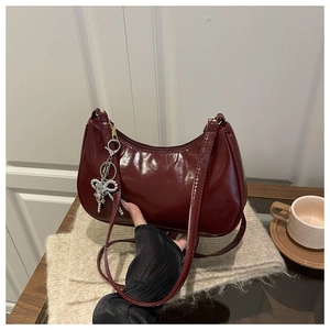 Detalle del bolso de media luna rojo oscuro con acabado brillante y colgante de lazo
