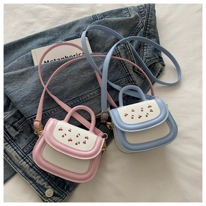 Detail of pink and blue cherry print crossbody bags on denim and book props