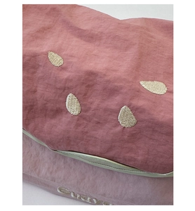 Close-up of pink crossbody bag featuring white embroidery and green contrast trim