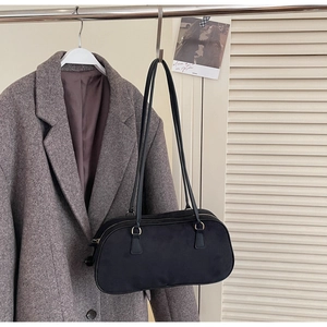 Minimalist black faux suede shoulder bag with silver zipper on a hanger against a coat