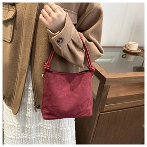 Detalle del bolso tote de ante burdeos con diseño de asa anudada y grabado de texto