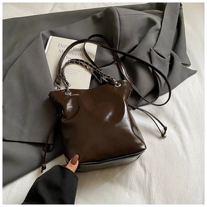 Detail of a dark brown glossy patent leather bucket bag with silver metal chain strap