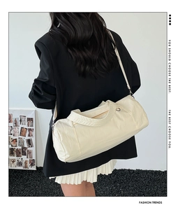 Détail du sac cylindrique en nylon beige porté en bandoulière par un mannequin