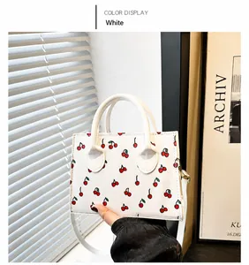 Detail of white square handbag with cherry print and circular metal handles
