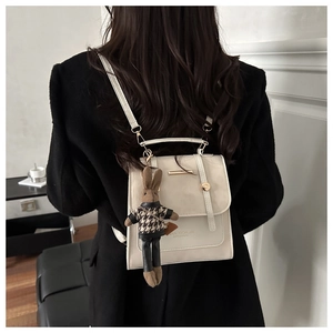 Primer plano de mochila de cuero blanco crema con barra dorada y colgante de conejo