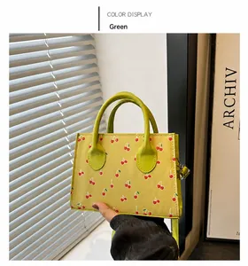Detail of green cherry print handbag with curved handles and detachable strap