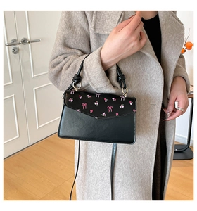 Détail d'un sac à main noir en similicuir avec imprimé floral rose et motifs de nœuds sur le rabat