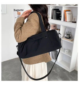 Large black nylon gym bag worn as crossbody by model in minimalist studio setting