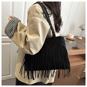 Detail of black faux suede bucket bag featuring long fringe and a woven shoulder strap