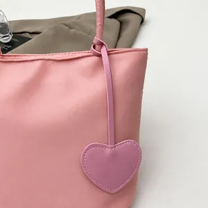 Detailed close-up of a pink nylon tote bag featuring a cute heart-shaped charm attachment