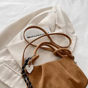 Close-up of brown suede dumpling bag with woven handle and heart charm on white fabric