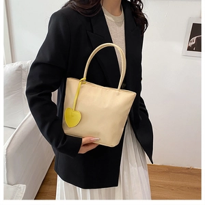Close-up of a beige nylon tote bag with a yellow heart leather pendant in a lifestyle setting