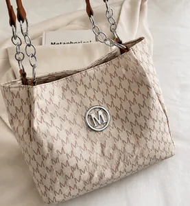 Detail of vintage beige tote bag with brown M-pattern texture and silver chain strap