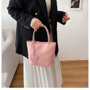 Detail view of a mini pink nylon handbag with a heart pendant held by a person