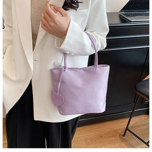 Close-up of a lilac nylon handbag with a heart-shaped charm held by a model in office wear