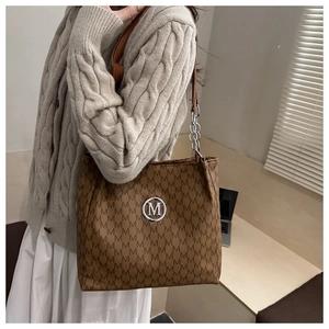 Detail of a brown monogram tote bag with a silver M logo and chain-link shoulder strap