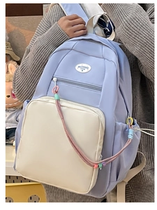 Dettaglio di zaino azzurro con tasca laterale e ciondoli colorati indossato da modella