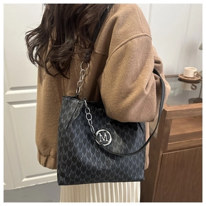 Detail of vintage monogram tote bag with silver M logo and chain strap on a model